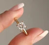 Gold ring with a diamond held by a hand against a neutral background