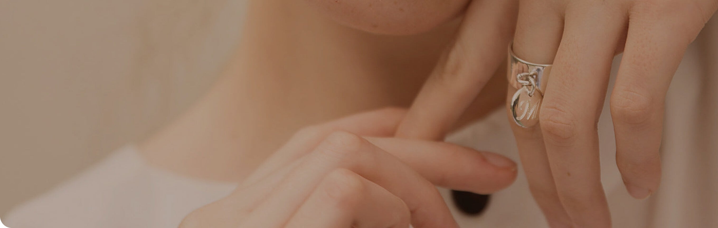 Close-up of a hand wearing a gold ring with a cat design on a neutral background