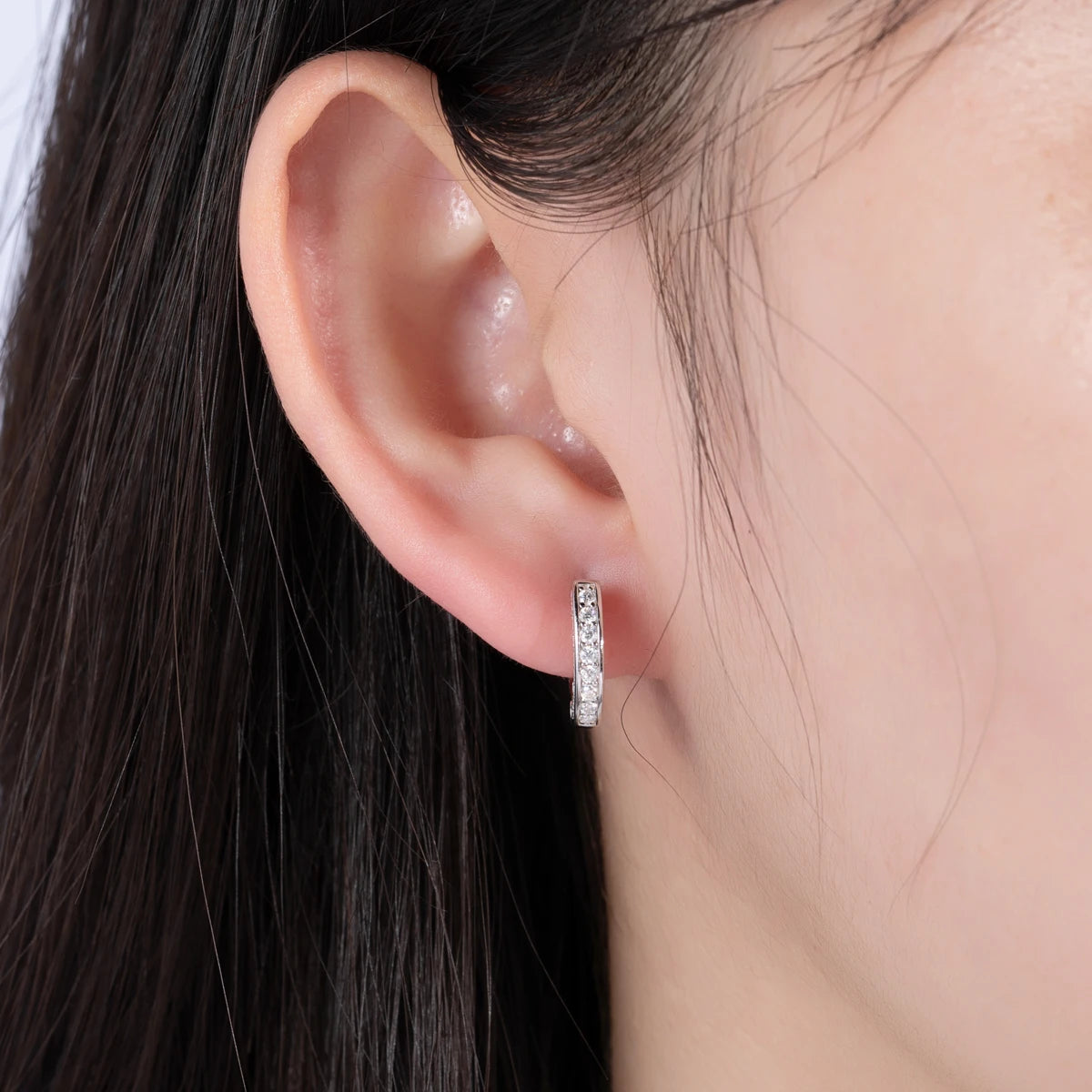 Close-up of an ear wearing a silver hoop earring with dark hair in the background