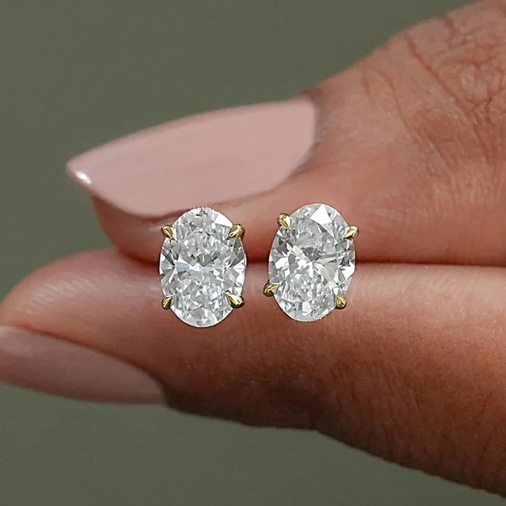 Diamond stud earrings held between fingers against a neutral background