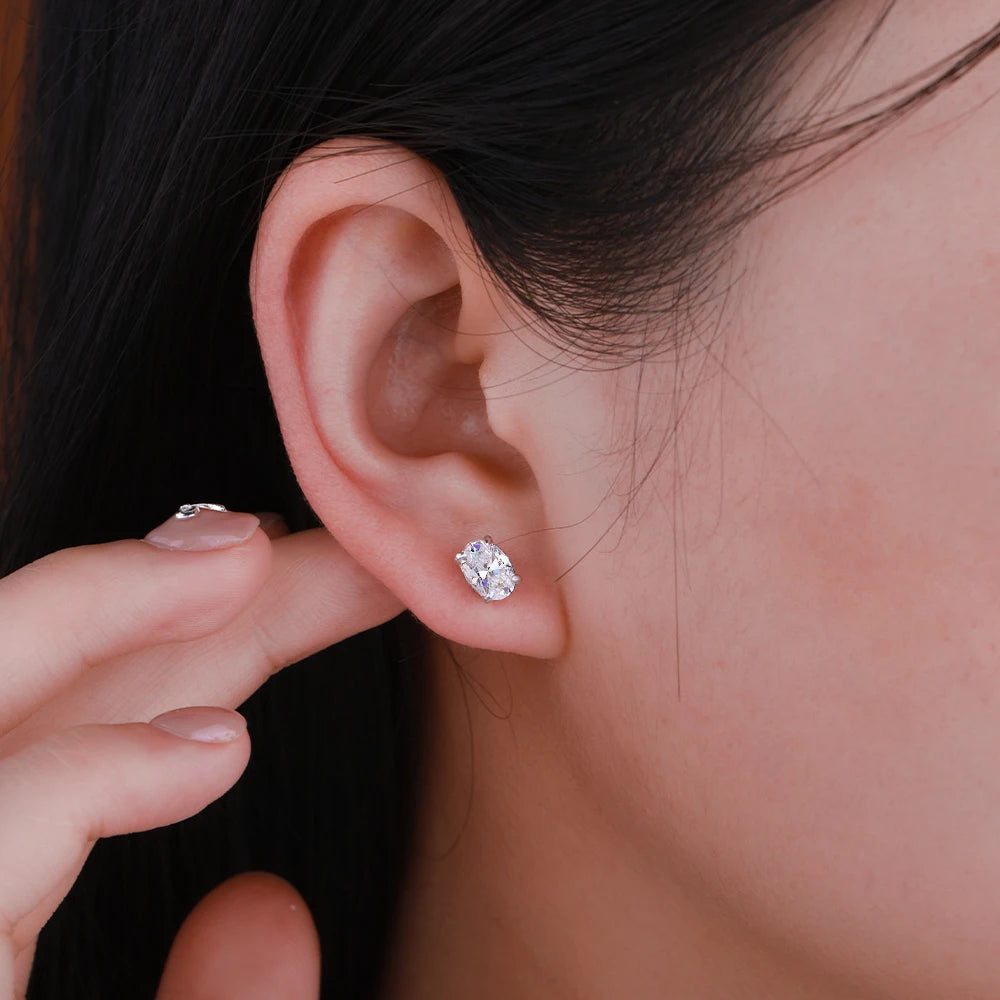 Close-up of an ear wearing a diamond earring with a hand pointing to it.