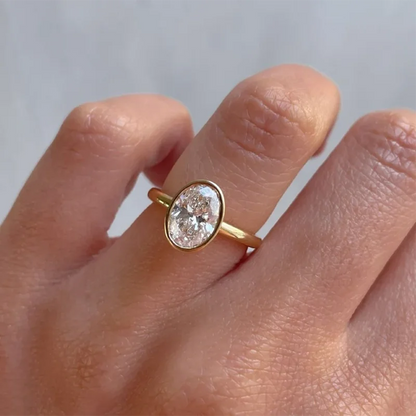 Gold ring with a diamond on a finger against a neutral background