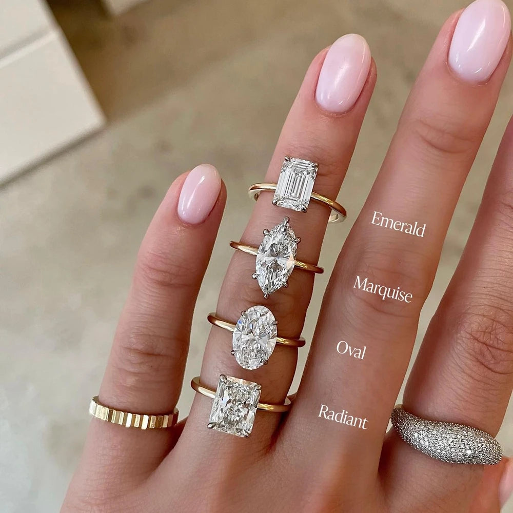 Hand wearing diamond rings with different shapes on a neutral background