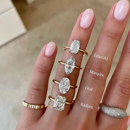 Hand wearing diamond rings with different shapes on a neutral background