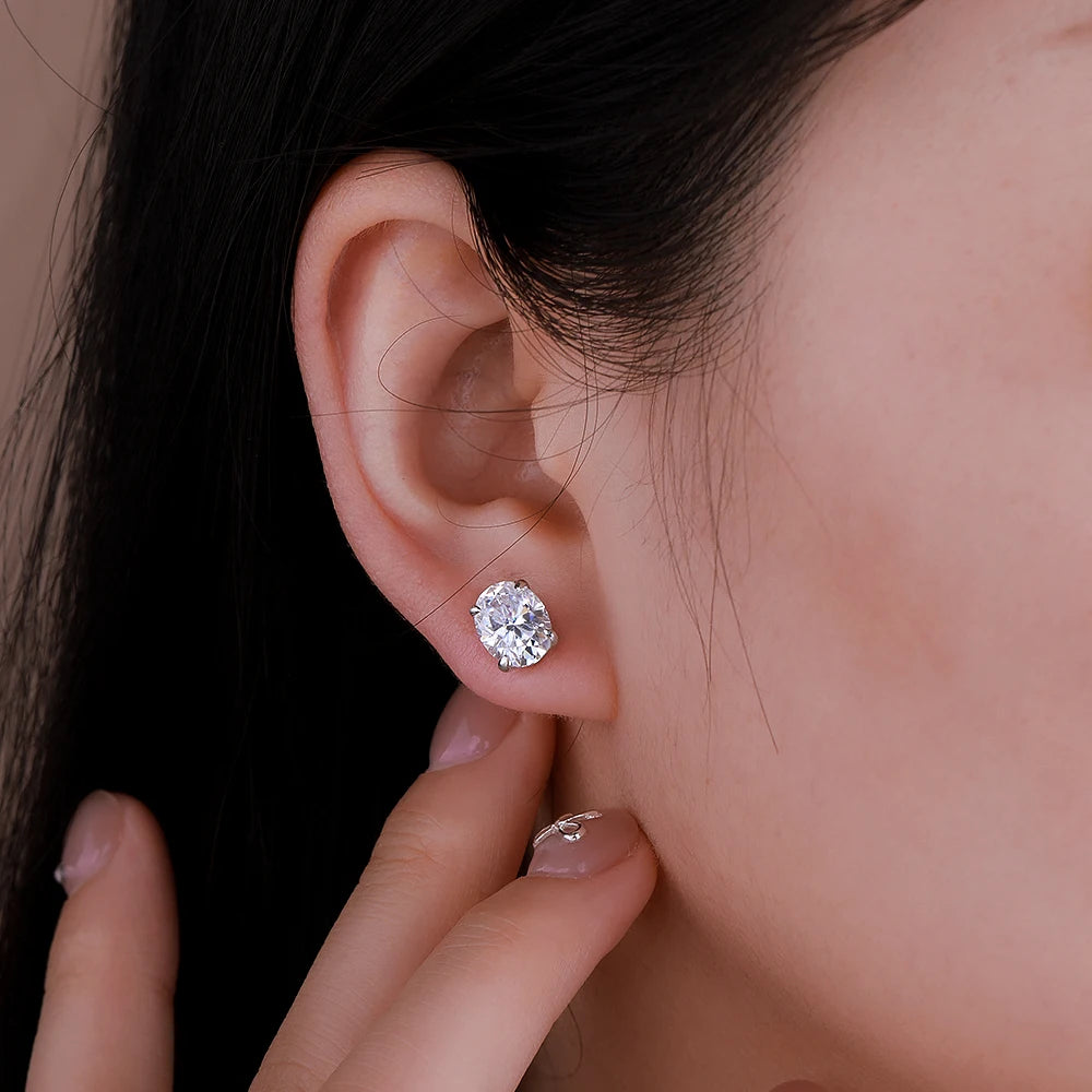 Close-up of a diamond earring being worn on an ear with a hand holding another earring.