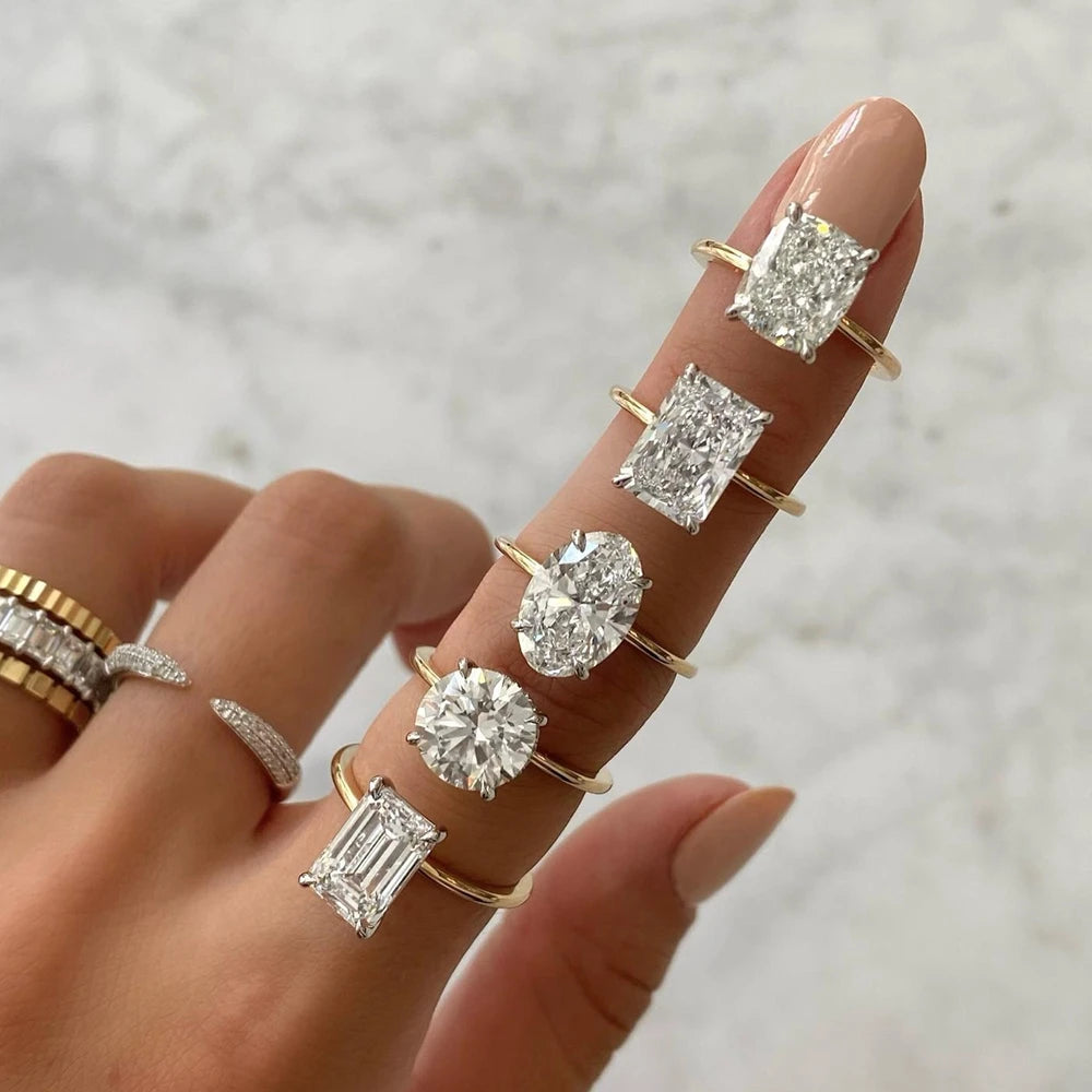 Hand wearing multiple gold rings with diamond stones on a neutral background