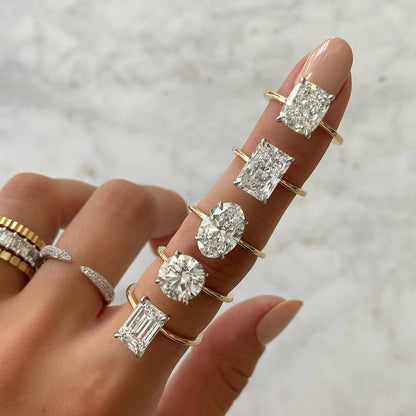 Hand wearing multiple gold rings with diamond stones on a neutral background