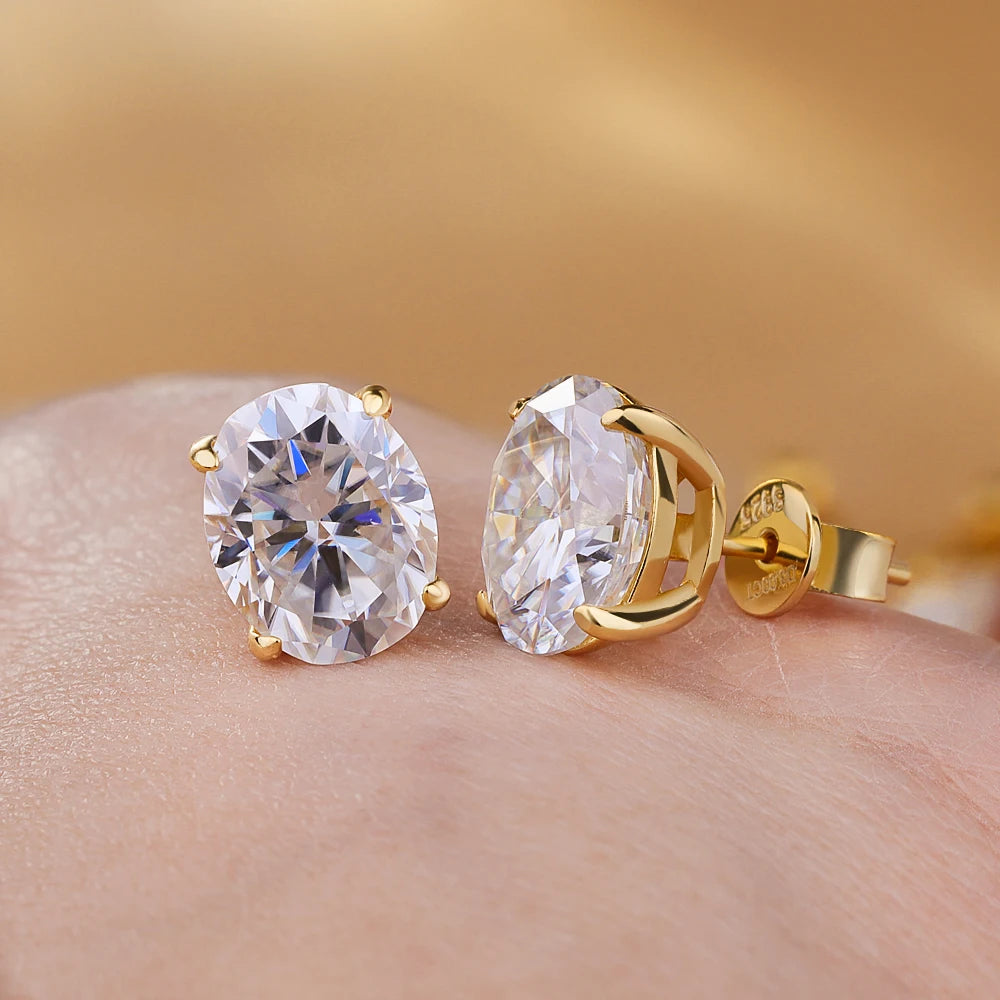 Gold earrings with large clear gemstones on a hand against a blurred gold background