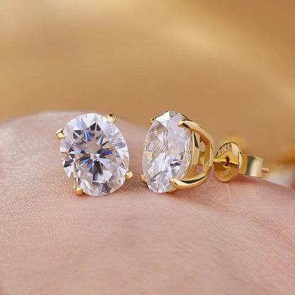 Gold earrings with large clear gemstones on a hand against a blurred gold background