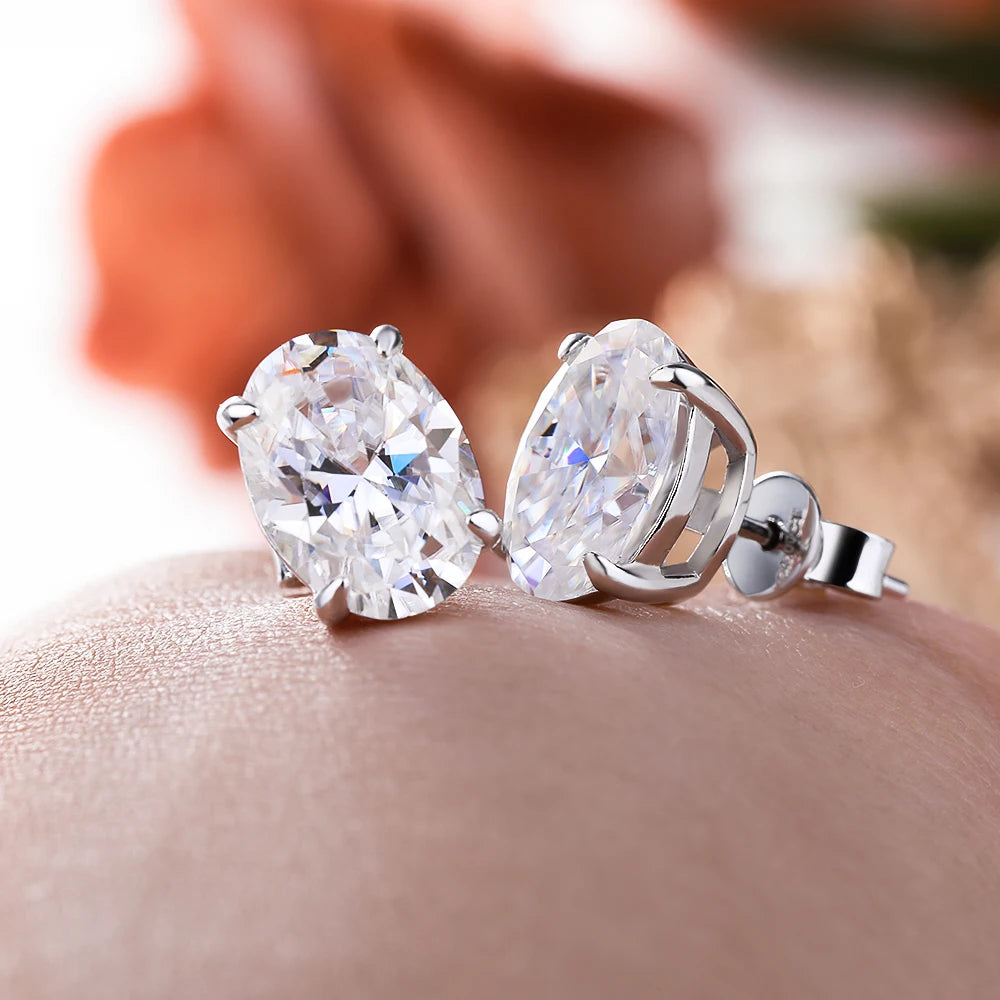 Pear-shaped diamond earrings on a person's ear with a blurred floral background