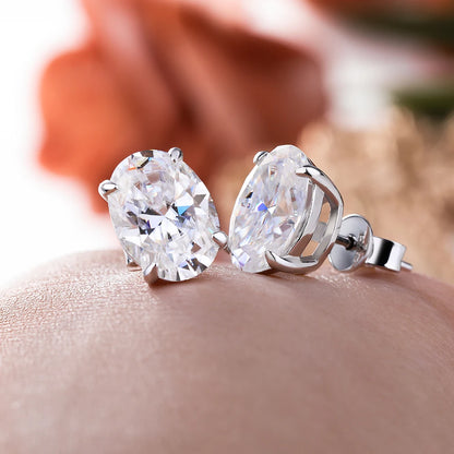 Pear-shaped diamond earrings on a person's ear with a blurred floral background