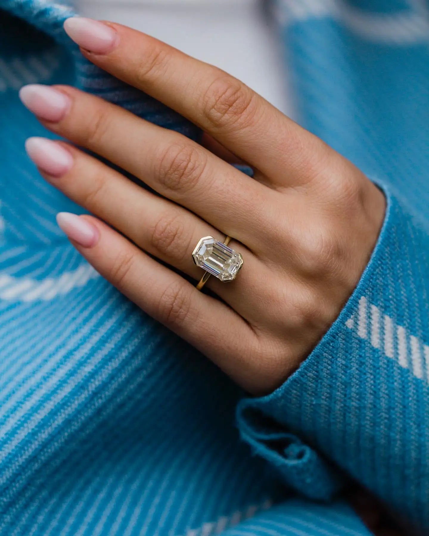 Hand wearing a diamond ring with a blue fabric background