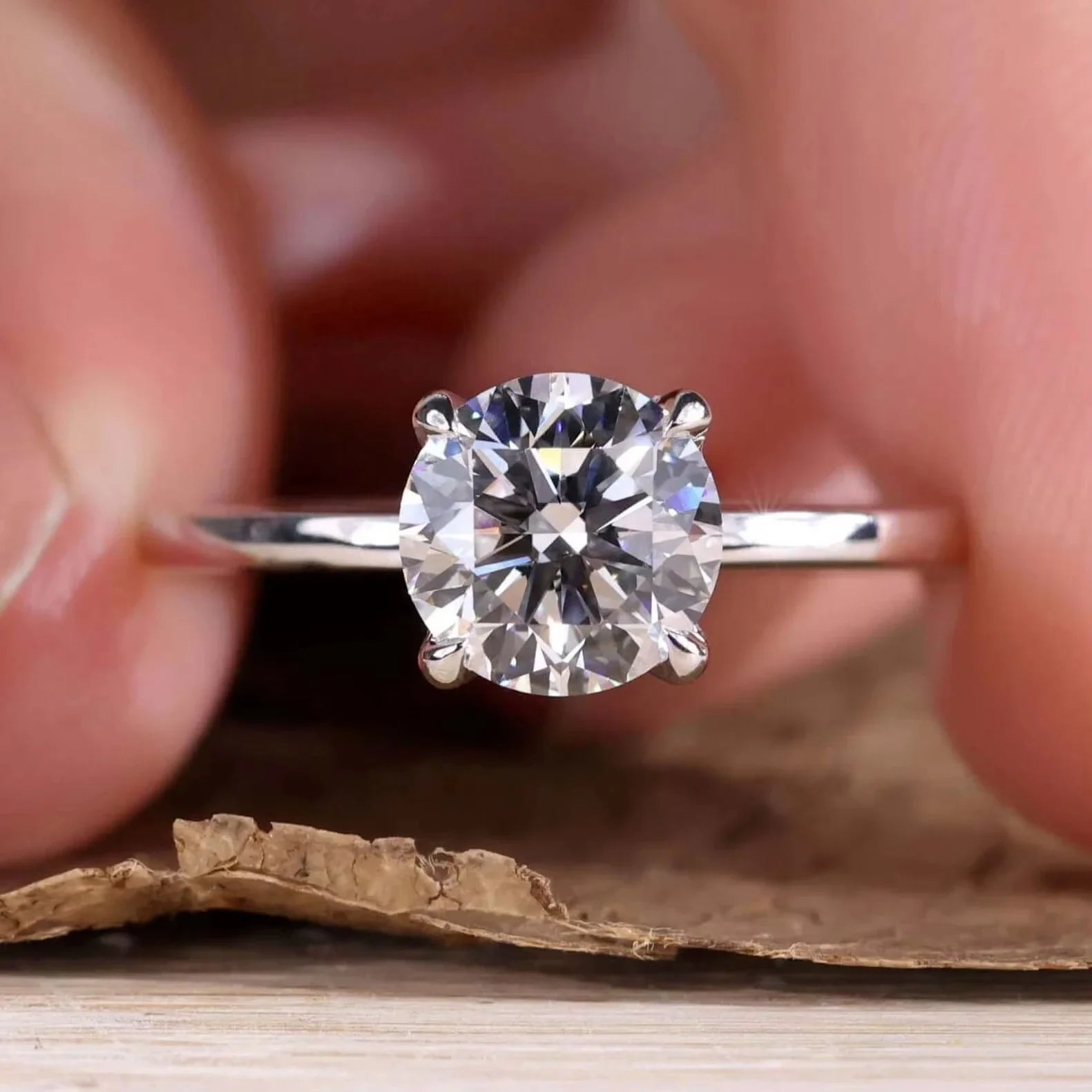 Diamond ring held between fingers with a blurred background