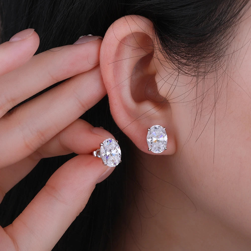 Close-up of a person wearing diamond earrings with a hand holding one in front of the ear.