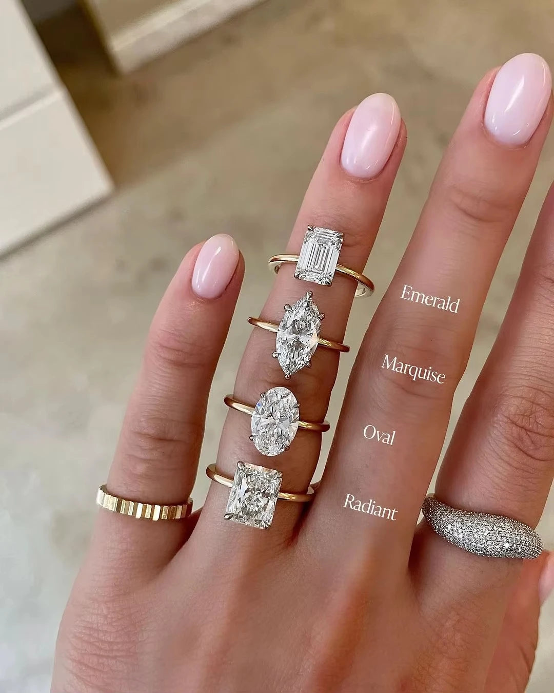 Hand wearing various diamond rings with different shapes on a neutral background