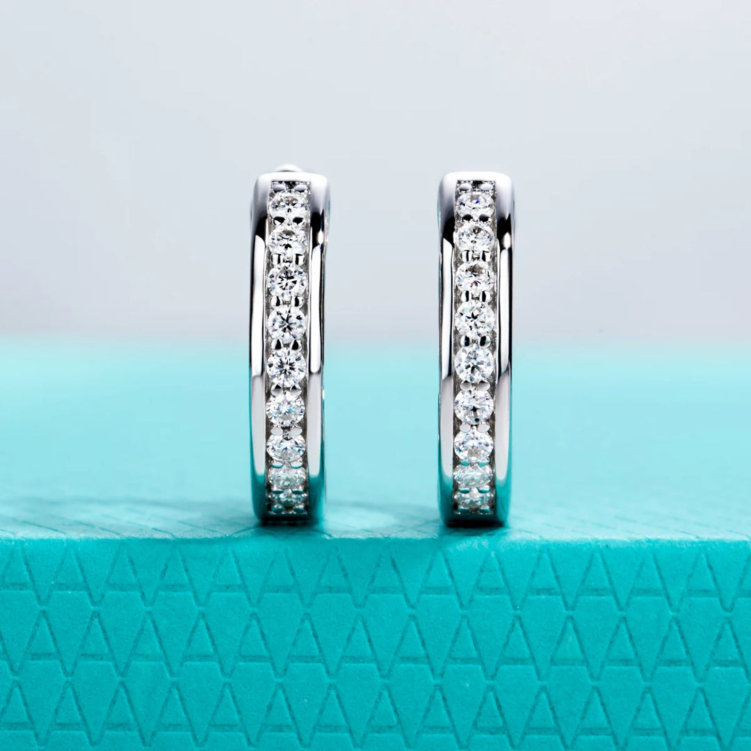 Pair of diamond hoop earrings on a textured teal surface with a light blue gradient background