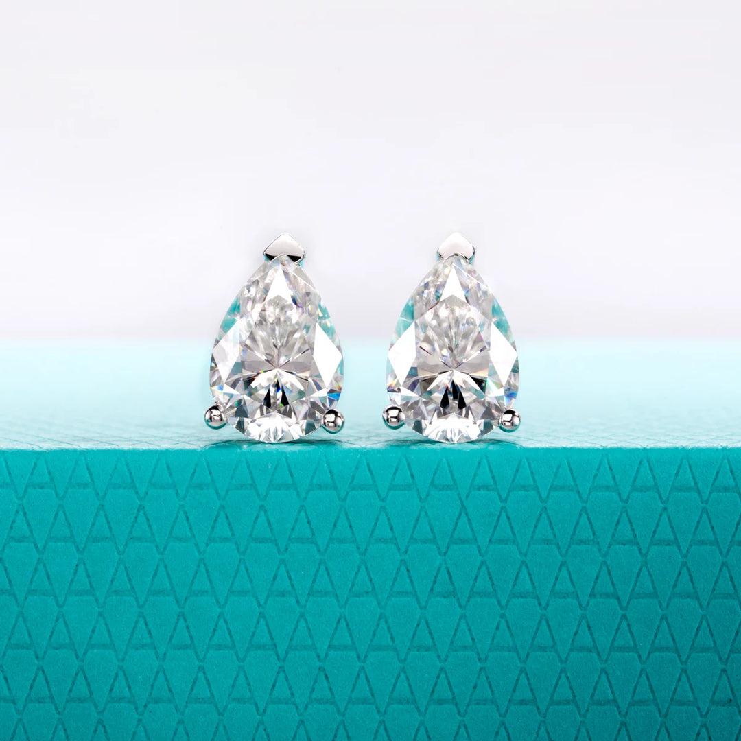 Pair of teardrop-shaped crystal earrings on a teal background with a geometric pattern.