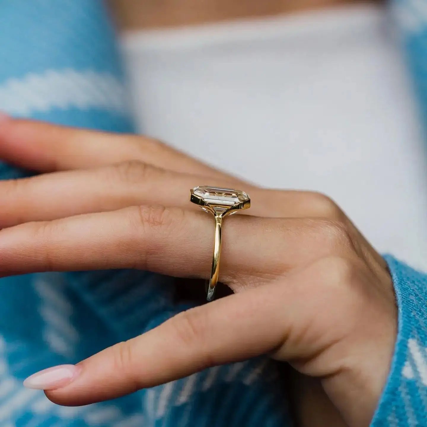 Gold ring on a finger with a blue patterned fabric background