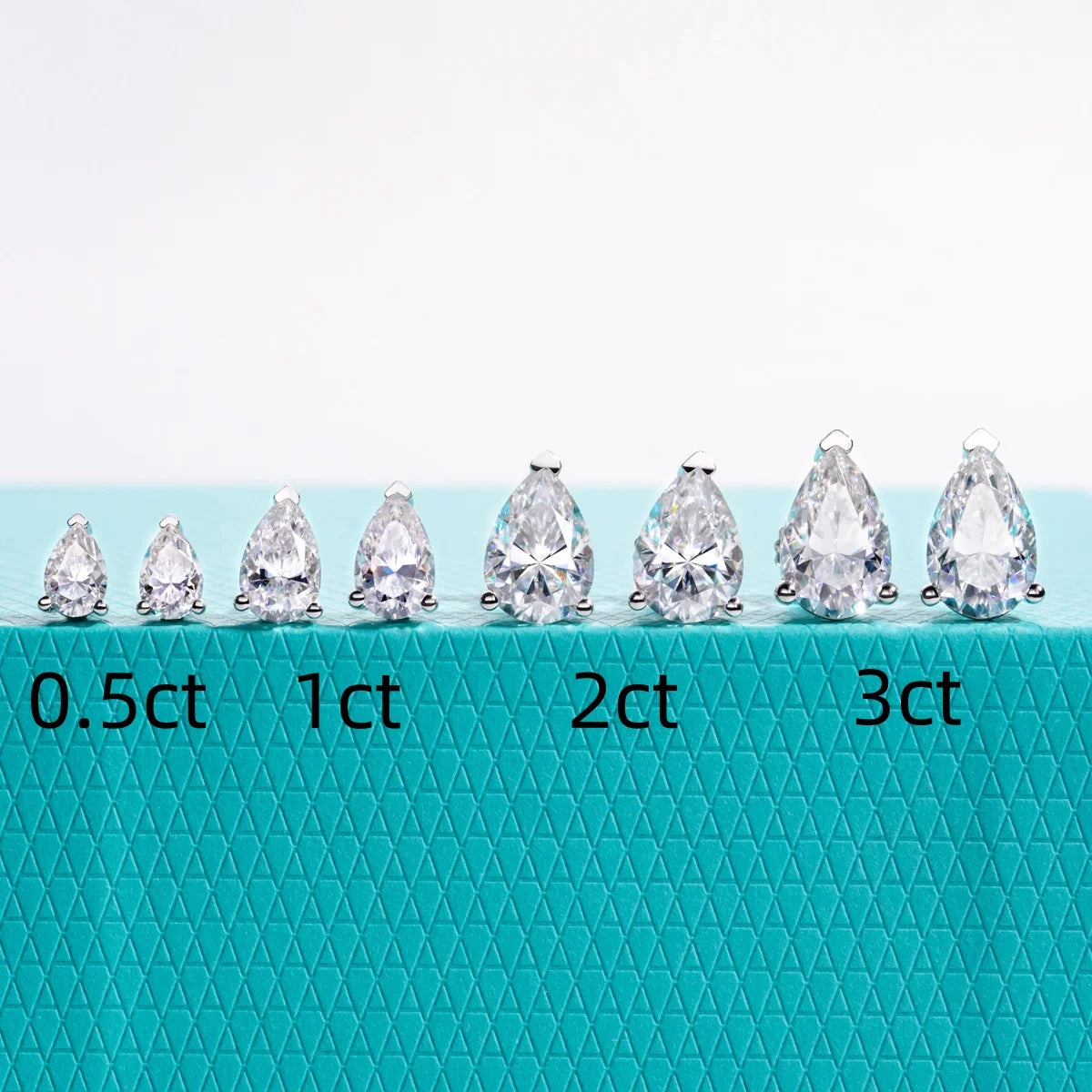 Teardrop-shaped diamonds of different carat weights on a teal background