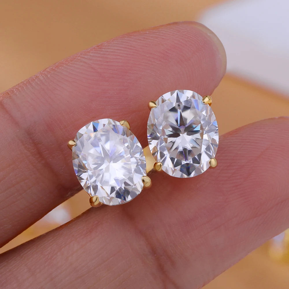 Gold earrings with large clear gemstones held between fingers against a blurred background