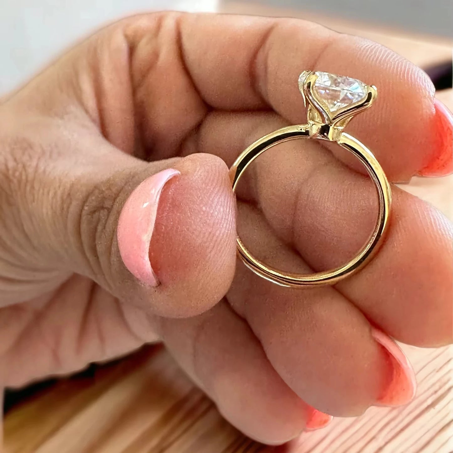 Gold ring with a large diamond held between fingers on a light background