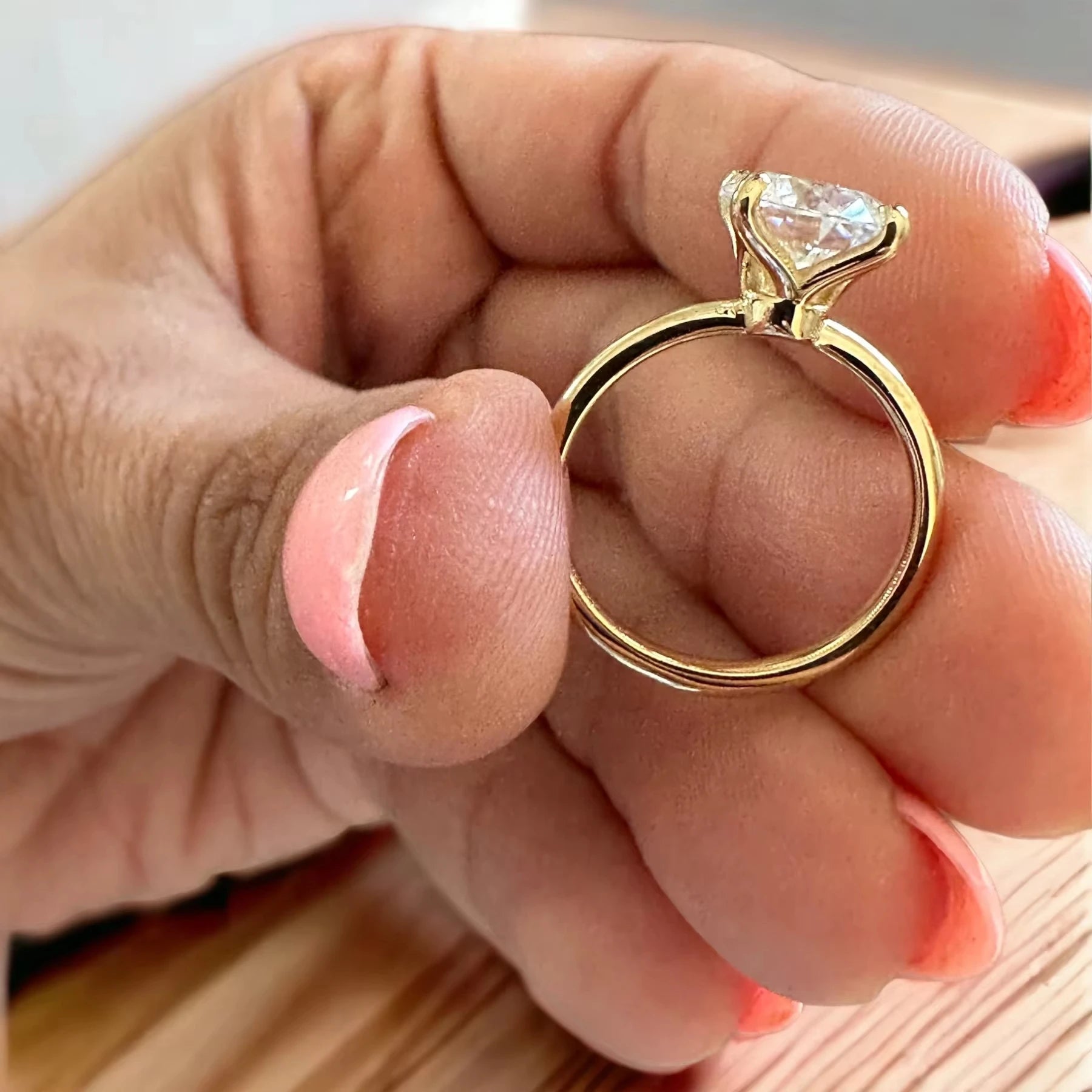 Gold ring with a large diamond held between fingers on a light background